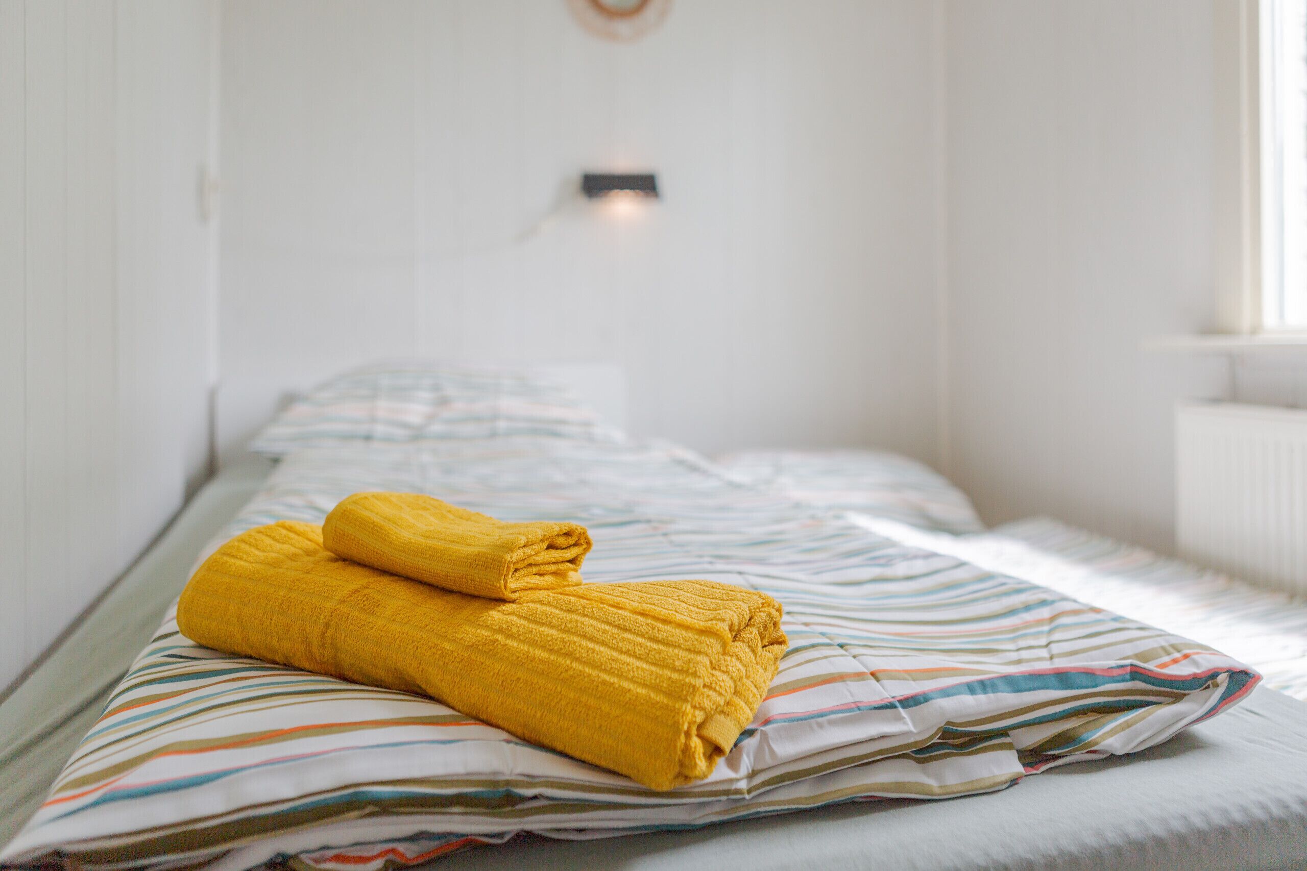 A single bed with a striped bedspread and two rolled-up towels.