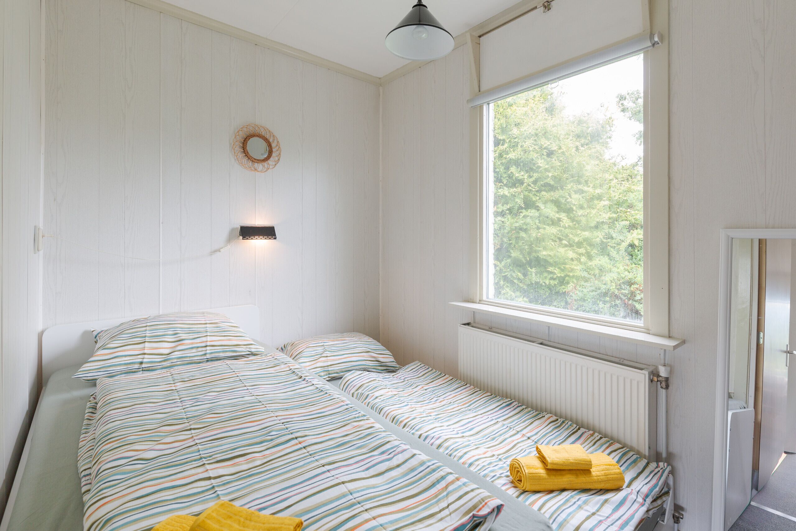 Ein Zimmer mit zwei Betten, einem Fenster, einer Wandleuchte und einem Heizkörper.