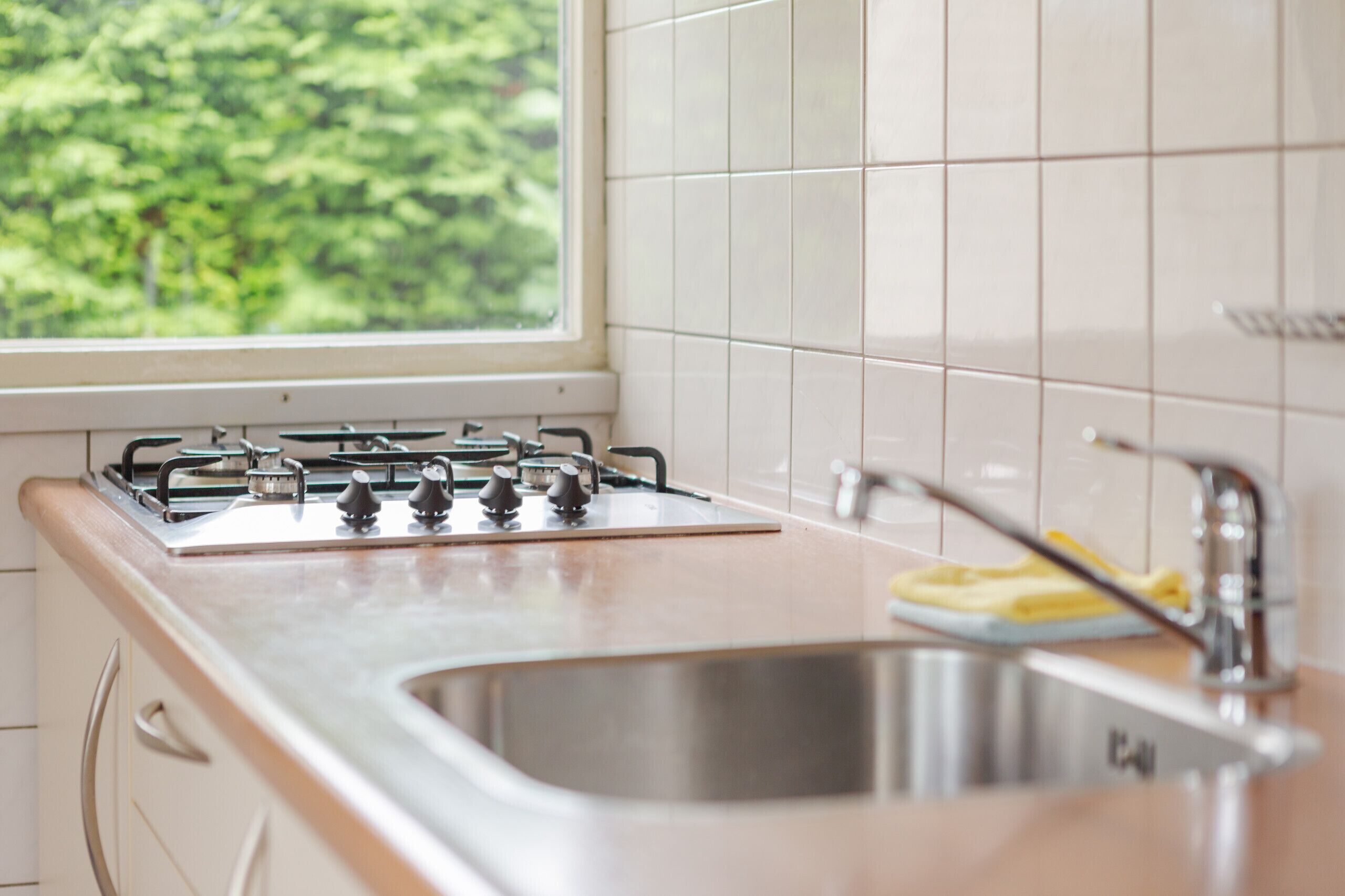 A kitchen with a gas stove, stainless steel sink, and a window with a view of greenery.