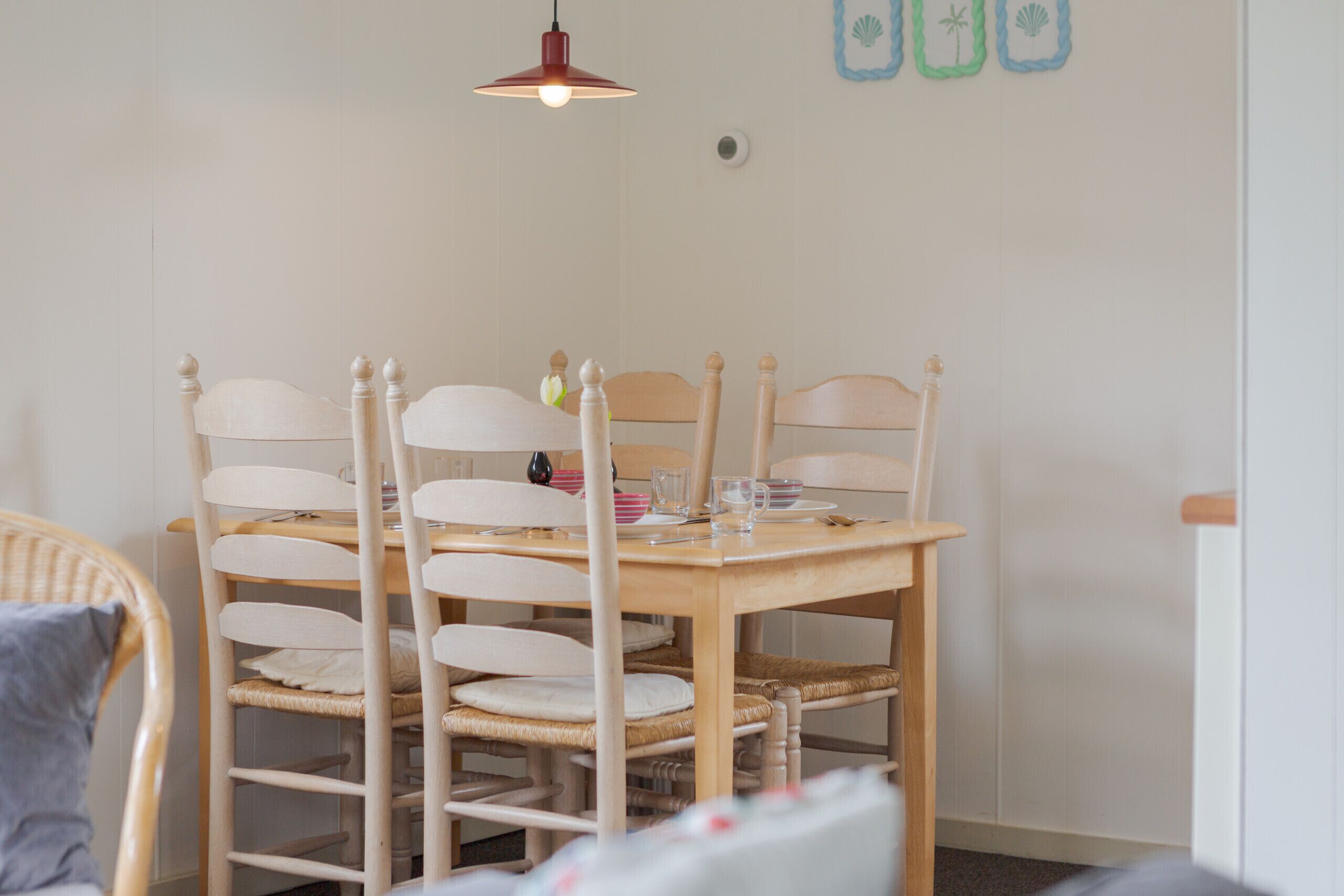 Een eethoek met een houten tafel en stoelen, een hangende hanglamp en een wand met decoratieve details.