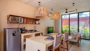 A modern kitchen with a refrigerator, microwave, and coffee maker. There is a dining area with a table and chairs. - Calixto 03 | Walk to Beach | Modern Design | Pool | Kitchen | Garden Oasis | Tranquil Setting (Bucerias)