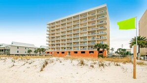 A multi-story hotel with a flat roof, located on a sandy beach with palm trees. - Seacrest 202 | Gulf-Front Condo w/ Balcony (Gulf Shores)