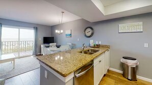 A modern kitchen with granite countertops, a sink, and a dining area with a table and chairs. - Seacrest 202 | Gulf-Front Condo w/ Balcony (Gulf Shores)