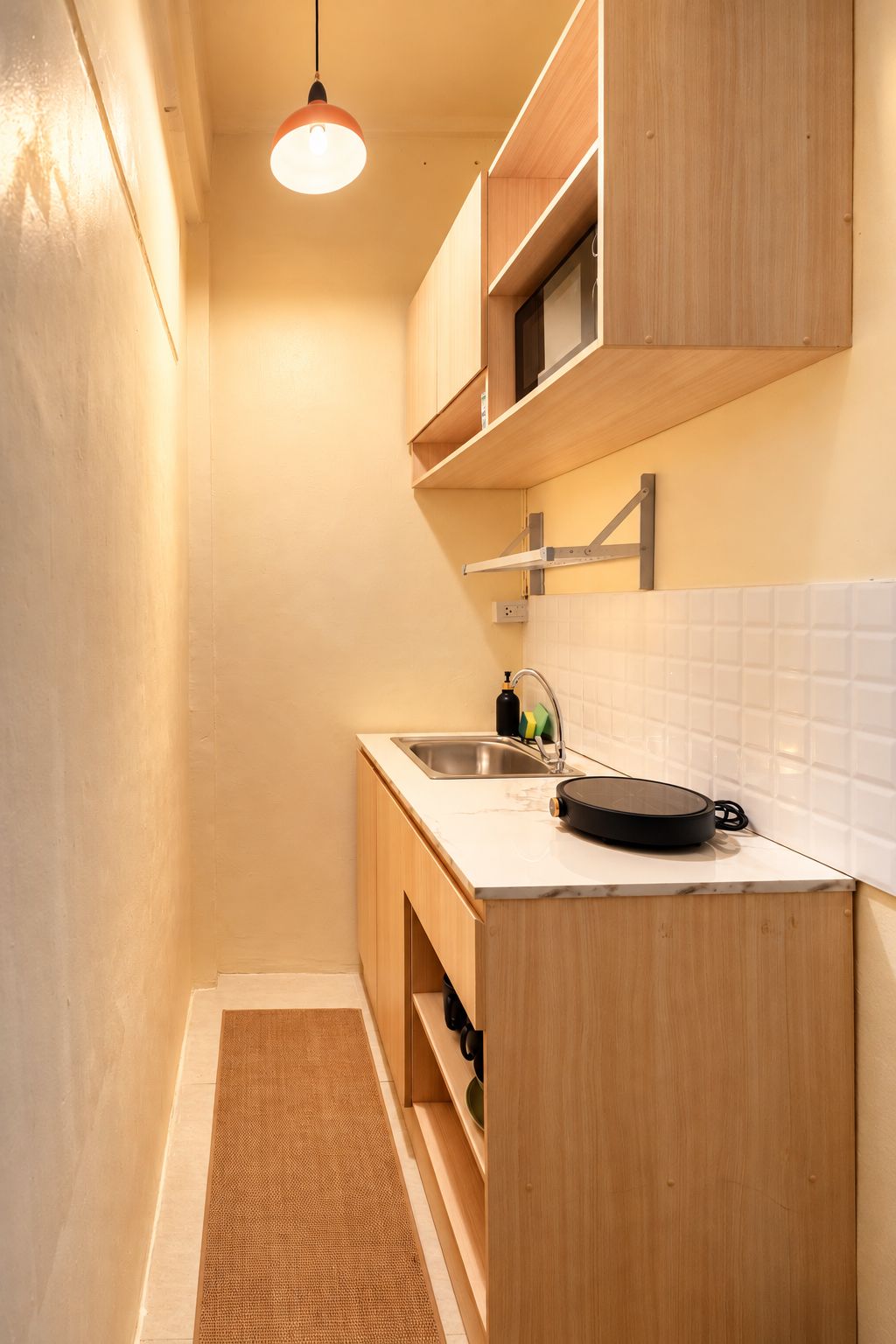 Una cocina estrecha con armarios de madera, una encimera, un fregadero y una lámpara colgante.