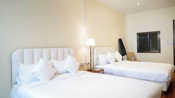 Hotellihuone, jossa on kaksi sänkyä, yöpöytä lampun kanssa, ikkuna ja ovi.