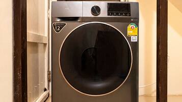A compact, modern washing machine in a narrow hallway with a tiled floor.