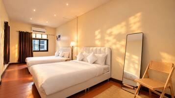 Habitación de hotel con dos camas, un espejo de pie, una silla de madera y una ventana con cortinas.