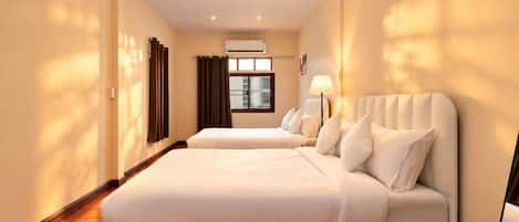 Una habitación de hotel con dos camas, una ventana con cortinas, un equipo de aire acondicionado y una lámpara.