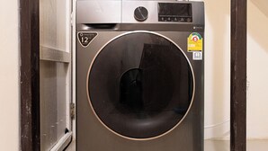 A compact, modern washing machine in a narrow hallway with a tiled floor and a blue pipe running along the wall. - House in Khao San - OH Homes Samsen 12 (Bangkok)