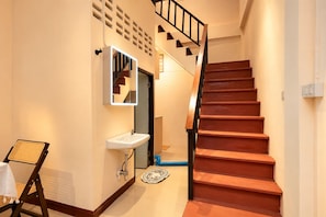 Una escalera con peldaños de madera y barandilla negra, que lleva a una habitación con pared blanca y un espejo.