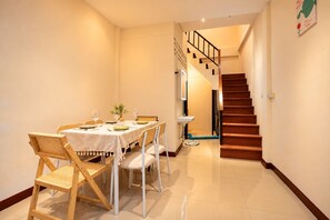A dining area with a table set for four, a staircase, and a wall-mounted artwork. - House in Khao San - OH Homes Samsen 12 (Bangkok)