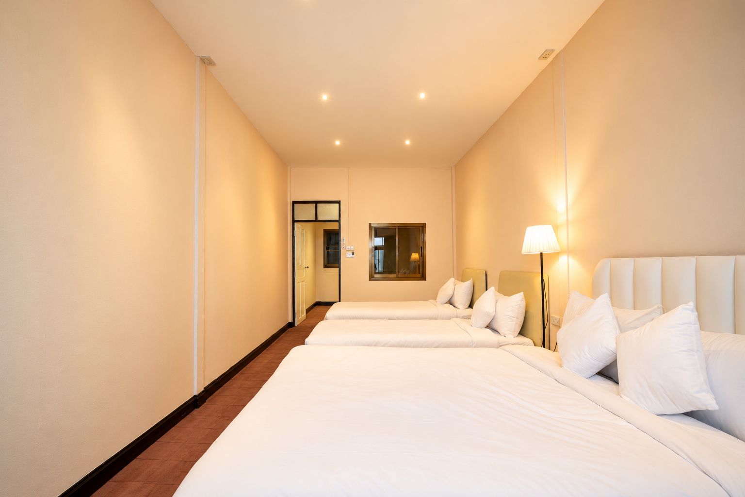 Ein Hotelzimmer mit zwei Betten, einer Tür, einem Spiegel und einem Nachttisch mit Lampe.