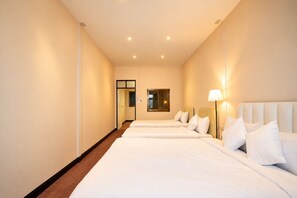 A hotel room with two beds, a door, a mirror, and a nightstand with a lamp. - House in Khao San - OH Homes Samsen 12 (Bangkok)