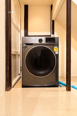 Una lavadora compacta y moderna en un pasillo estrecho con suelo de baldosas.