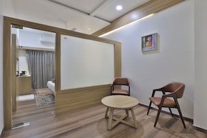 A modern room with a wooden floor, a round table, two brown chairs, a white sofa, and a sliding door leading to a bathroom.