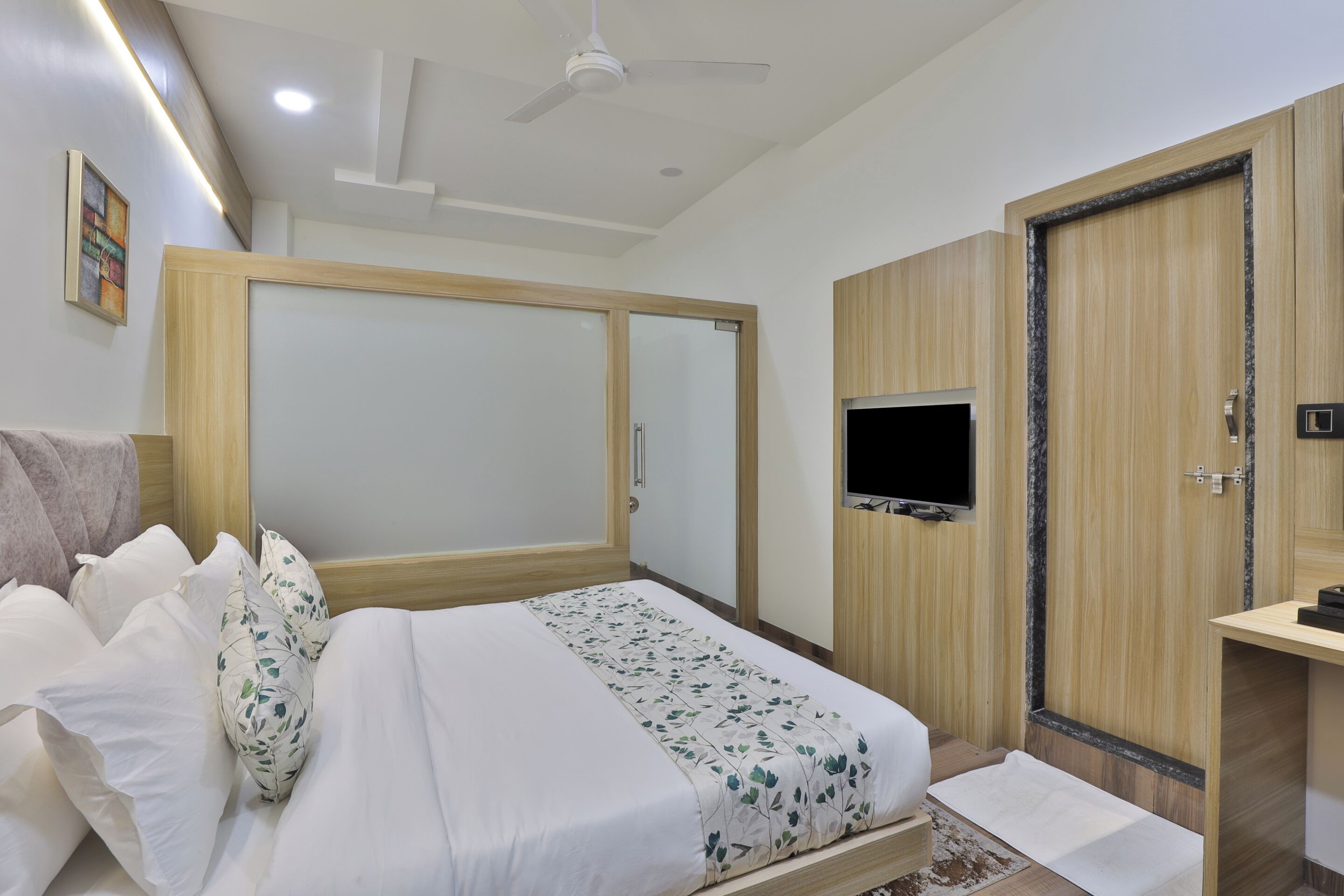 A bedroom with a bed, a wardrobe, a television, and a ceiling fan.