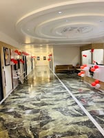 A hotel corridor with a marble floor, a reception desk with red and white balloons, and framed pictures on the walls.