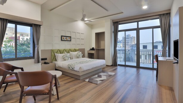 A modern hotel room with a large bed, a desk, a chair, and a balcony with a city view. - Hotel SR Laxmi (Anand)
