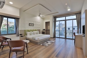A modern hotel room with a large bed, a desk, a chair, and a balcony with a city view.