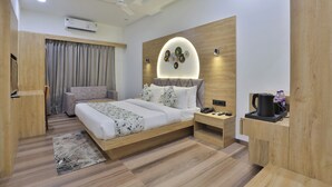 A modern bedroom with a wooden bed, a nightstand, a desk, and a wall-mounted light fixture. - Hotel SR Laxmi (Anand)