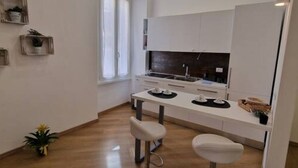A modern kitchen with white cabinetry, a central island, and two bar stools. - Ultramarine neptune (Nettuno)