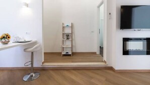 A modern kitchen with a white countertop, a bar stool, a wooden ladder shelf, and a TV mounted on the wall. - Ultramarine neptune (Nettuno)