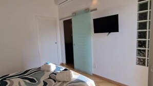 A bedroom with a bed, a TV mounted on the wall, a door, and a window with blinds. - Ultramarine neptune (Nettuno)