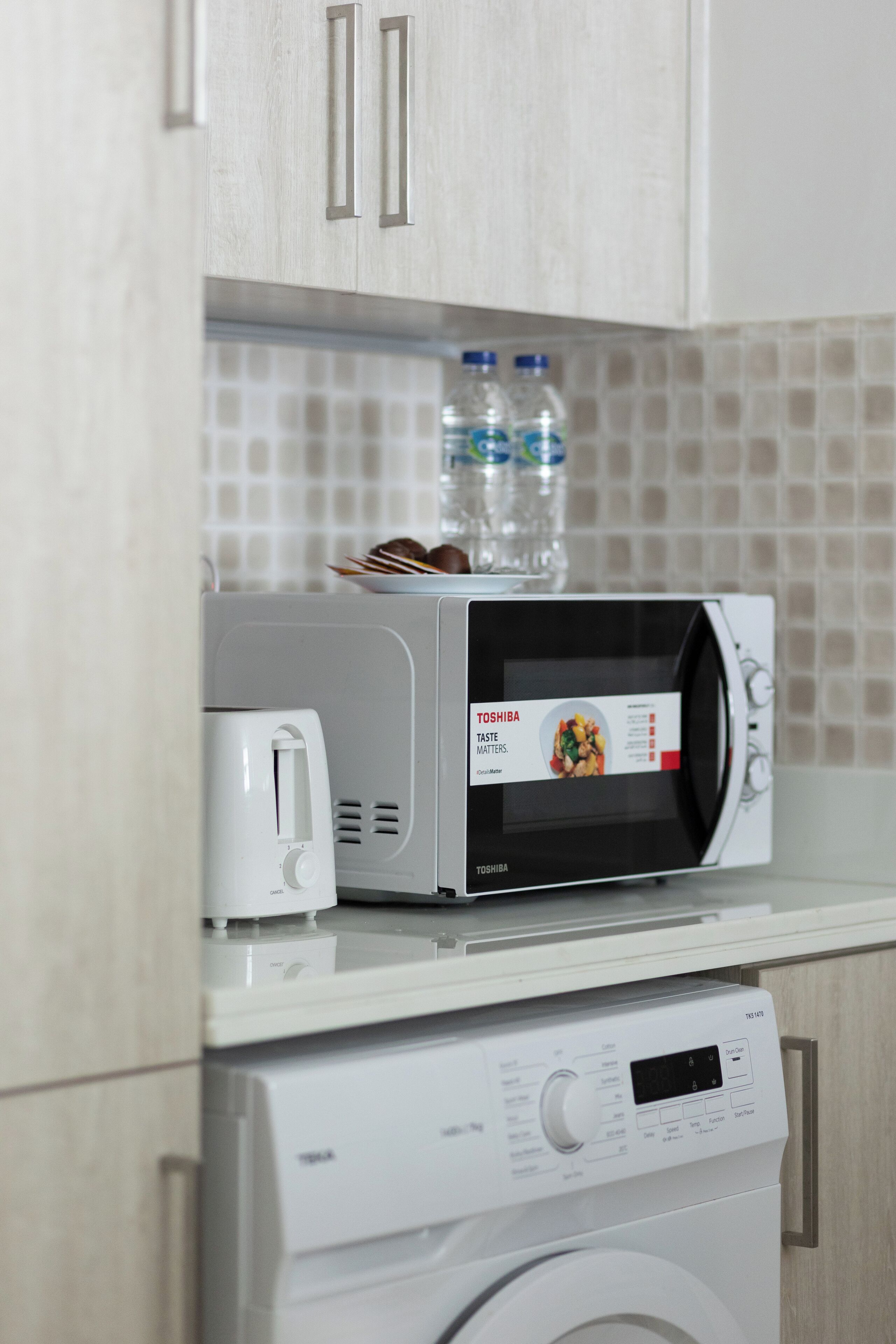A compact kitchen with a microwave, toaster, and washing machine.