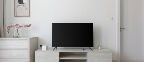 A modern living room with a flat-screen TV on a wooden stand, a vase with flowers, and a white door.