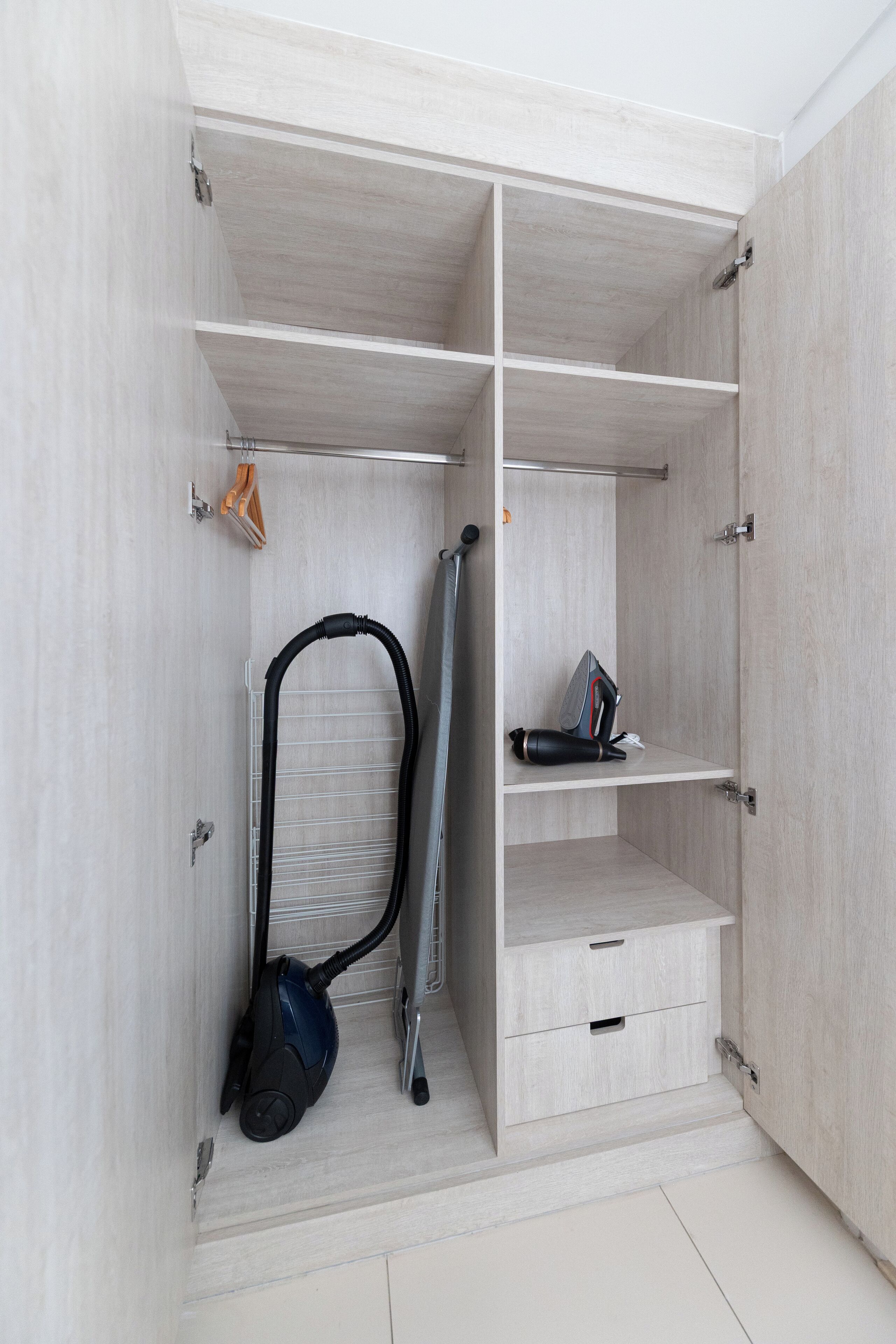 Un dressing accessible sans porte, doté d’étagères ouvertes, un aspirateur et une chaise pliante.