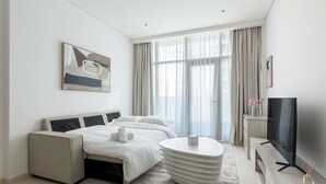 A modern hotel room with a bed, a sofa, a TV, and a large window with curtains.