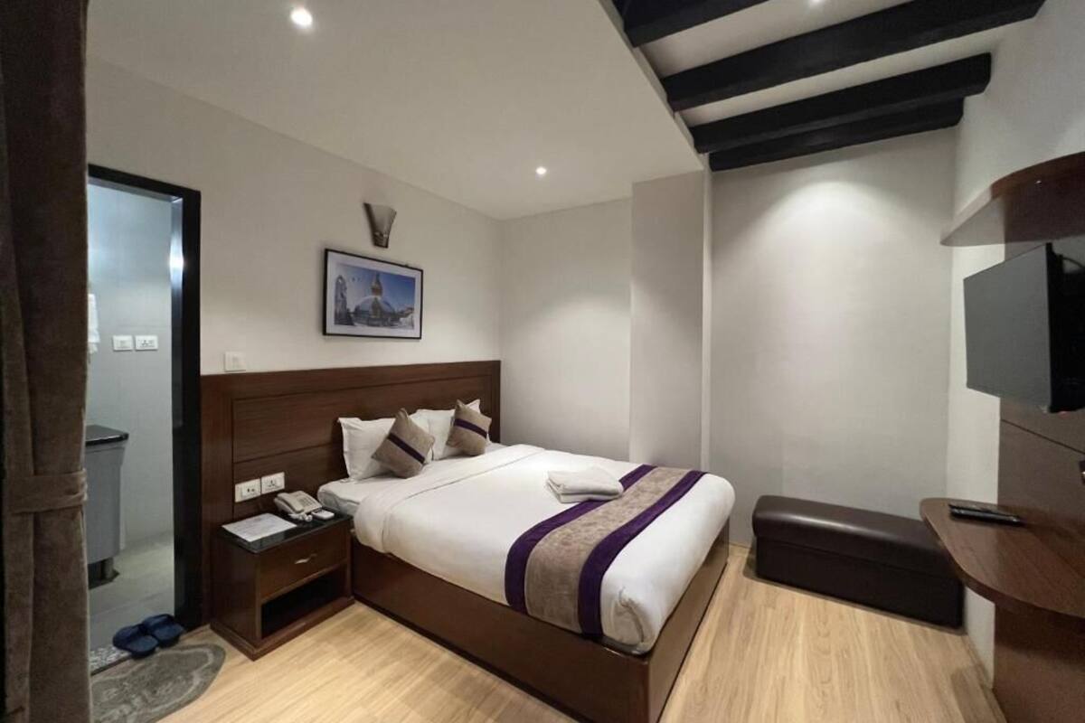 Una habitació d'hotel moderna amb un llit de fusta, una tauleta de nit amb un telèfon, un escriptori petit i una banca.