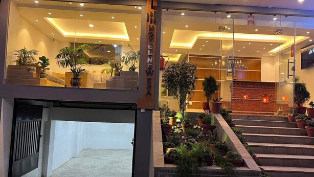 A hotel entrance with a modern design, featuring a glass facade, a staircase with potted plants, and a reception area with a wooden accent wall. - Hotel New Era (Kathmandu)