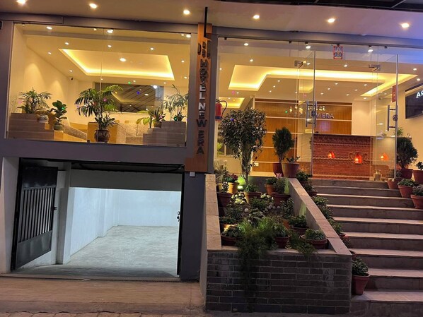 A hotel entrance with a modern design, featuring a glass facade, a staircase with potted plants, and a reception area with a wooden accent wall. - Hotel New Era (Kathmandu)