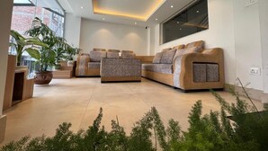 A modern living room with a sectional sofa, a large window, and a potted plant. - Hotel New Era (Kathmandu)