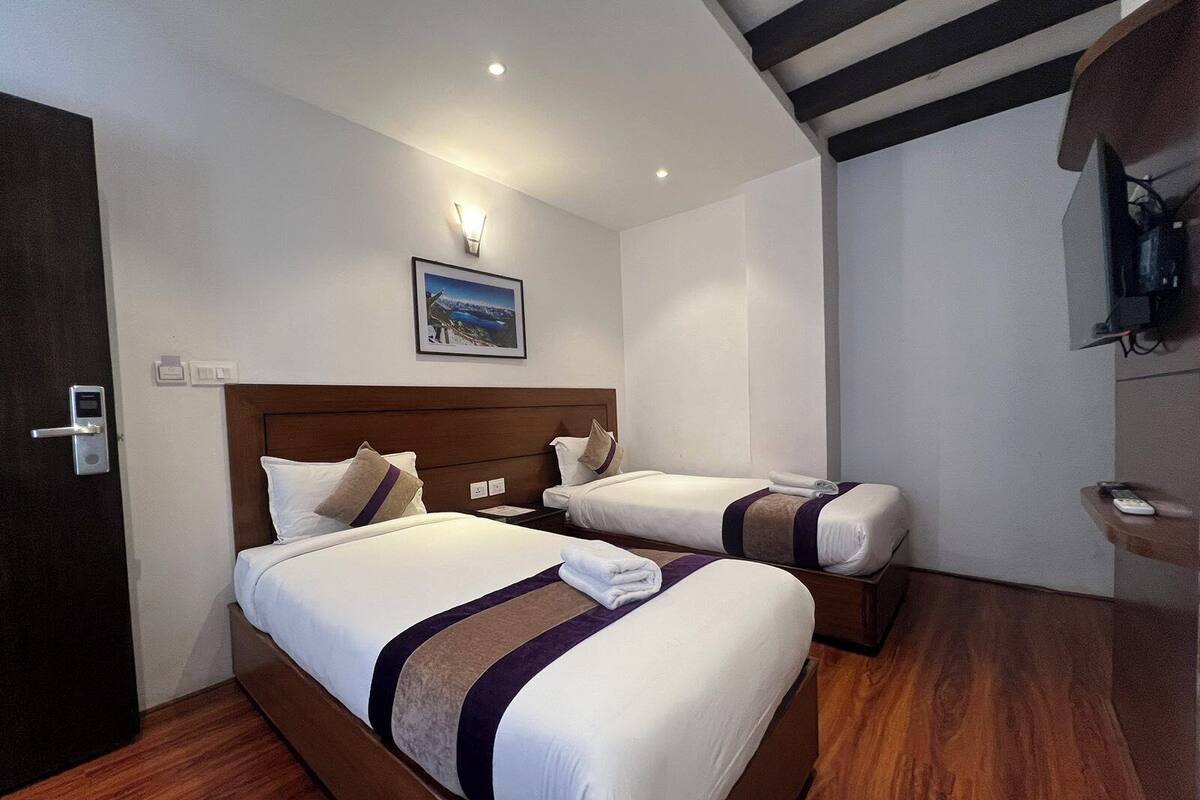 Habitació d'hotel amb dos llits, un terra de fusta, un televisor fixat a la paret i una pintura d'un paisatge.