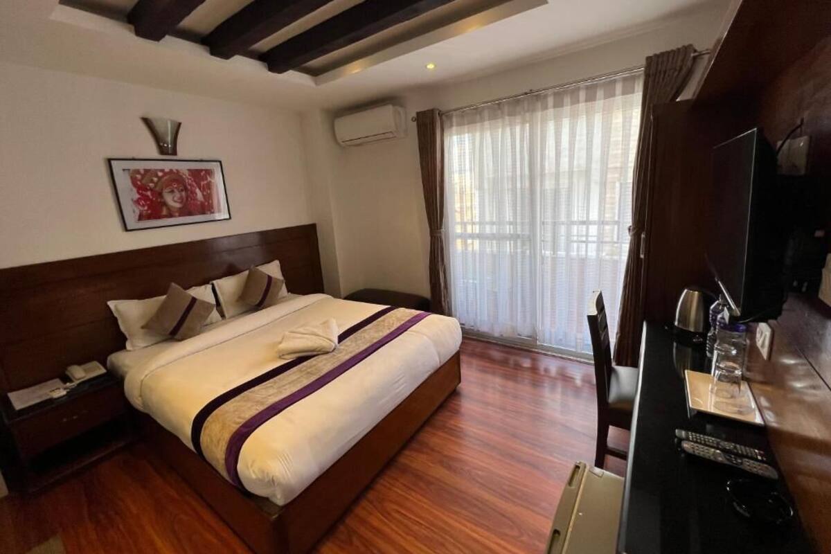 Habitació d'hotel amb un llit gran, televisió, escriptori i finestra amb cortines.