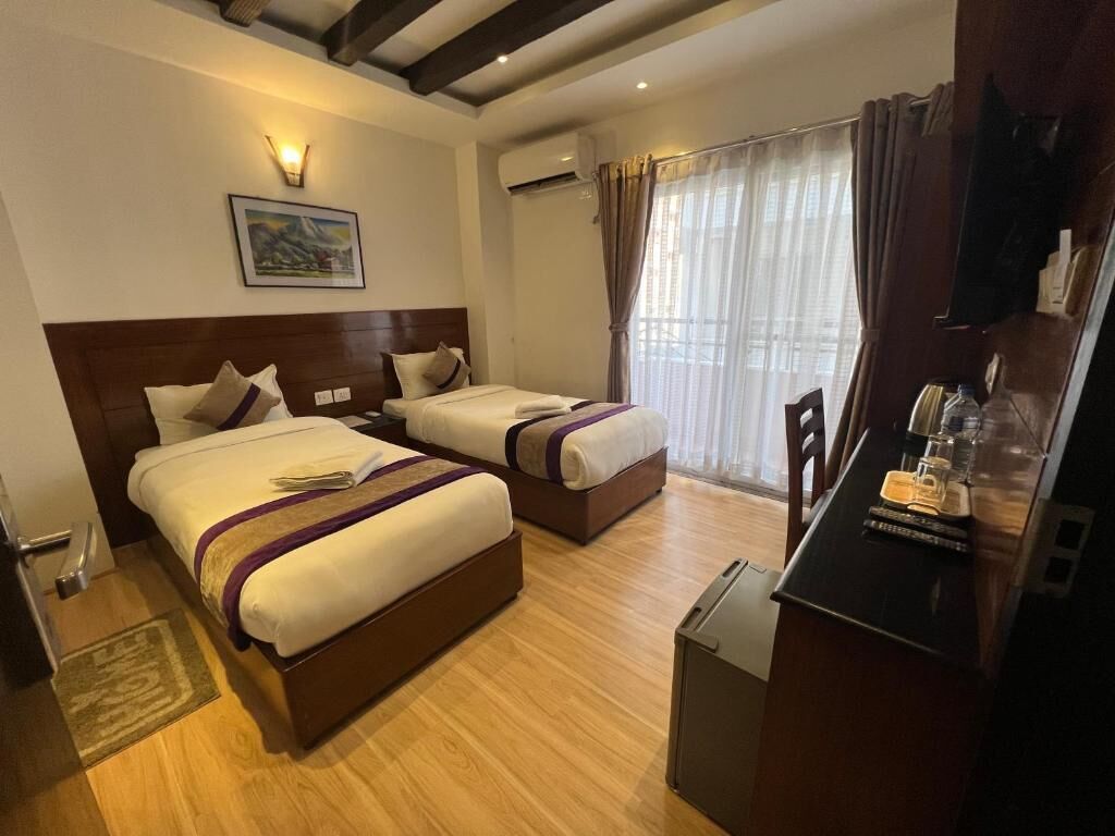 A hotel room with two beds, a desk, a chair, a TV, and a window with curtains.