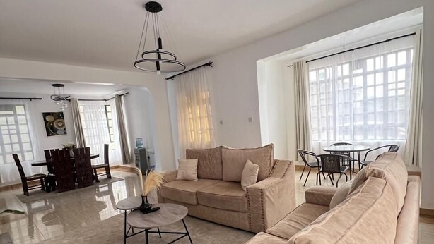 A spacious living room with a beige sofa, a round coffee table, and a dining area with a table and chairs. - Lux Suites The comfort Place Naivasha (Naivasha)