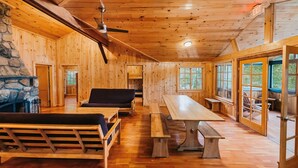 A wooden cabin interior with a stone fireplace, wooden benches, a dining table, and large windows. - Harriman Outdoor Center - Cranberry Cabin (Haverstraw)