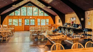 Un amplio comedor con mesas y sillas de madera, una barra de buffet y grandes ventanales que dejan entrar luz natural.
