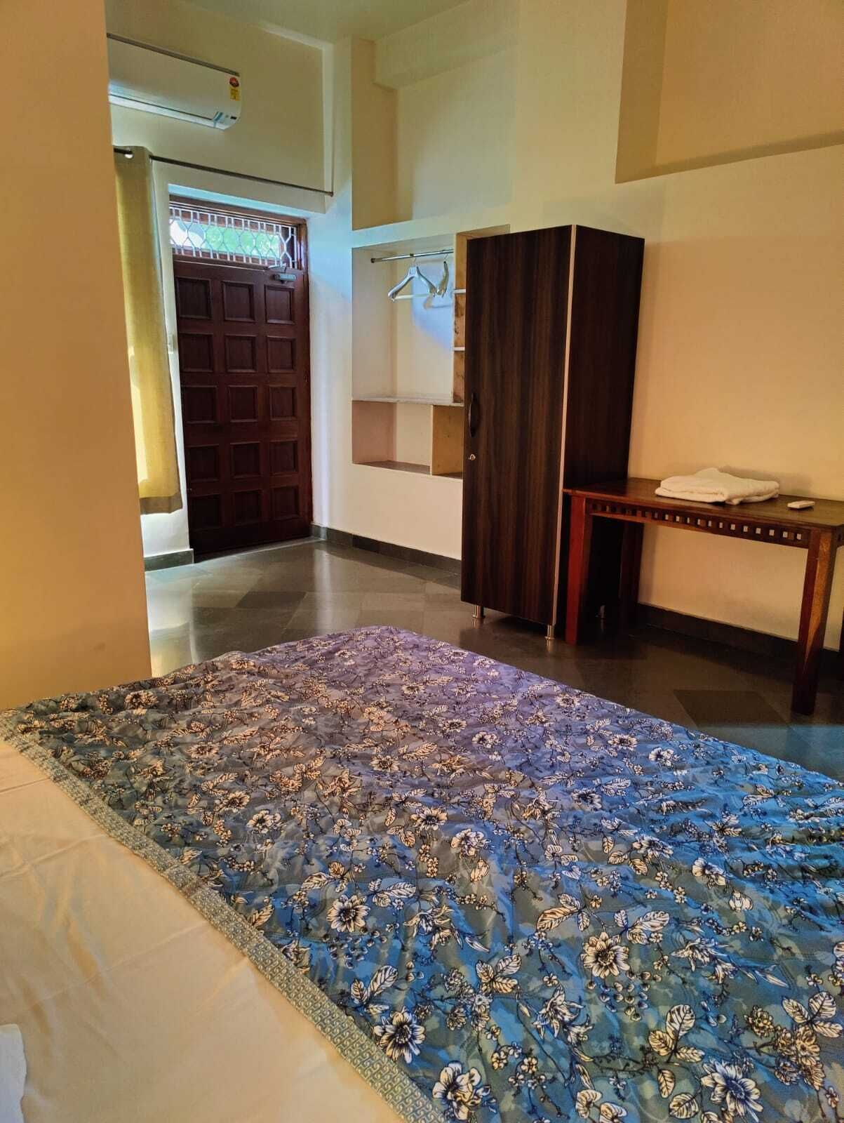 A room with a large bed, a wooden wardrobe, a small table with a towel, and a door leading to another room.