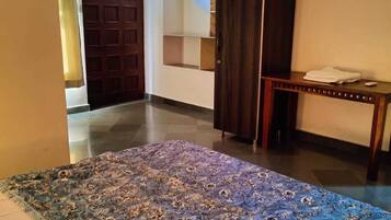 A room with a large bed, a wooden wardrobe, a small table with a towel, and a door leading to another room.