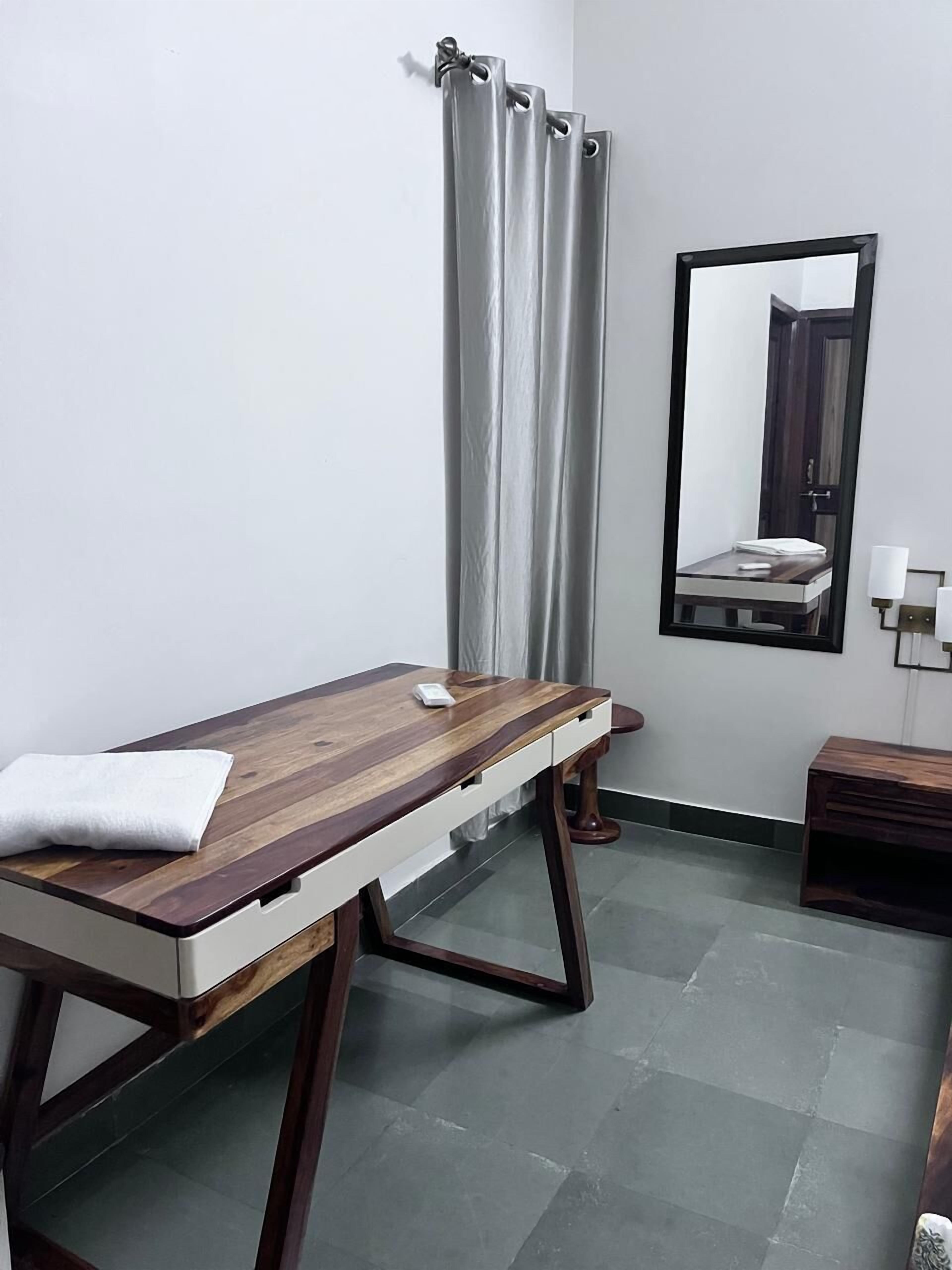 A room with a wooden massage table, a small bedside table, a mirror, and a curtain.