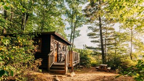 Eine rustikale Holzhütte mit einer Holzterrasse und einem Picknicktisch in einem bewaldeten Gebiet.