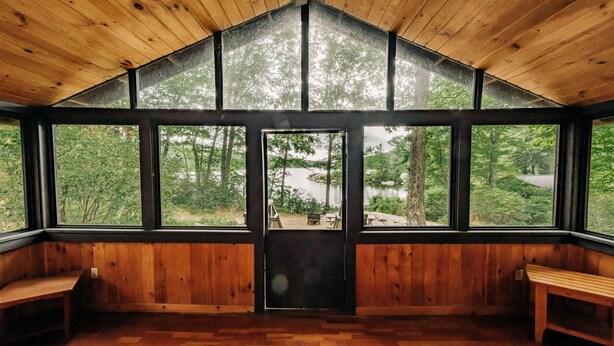 Eine Holzhütte mit großen Fenstern, einer Holzbank und Blick auf den Wald.