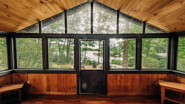 Una cabaña de madera con ventanas grandes, un banco de madera y vistas al bosque.