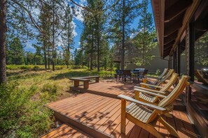 A wooden deck with outdoor seating, surrounded by trees and a clear sky. - Sleeps 14+ | 7 bed, 6 bath | SHARC | EV | Peloton (Sunriver)