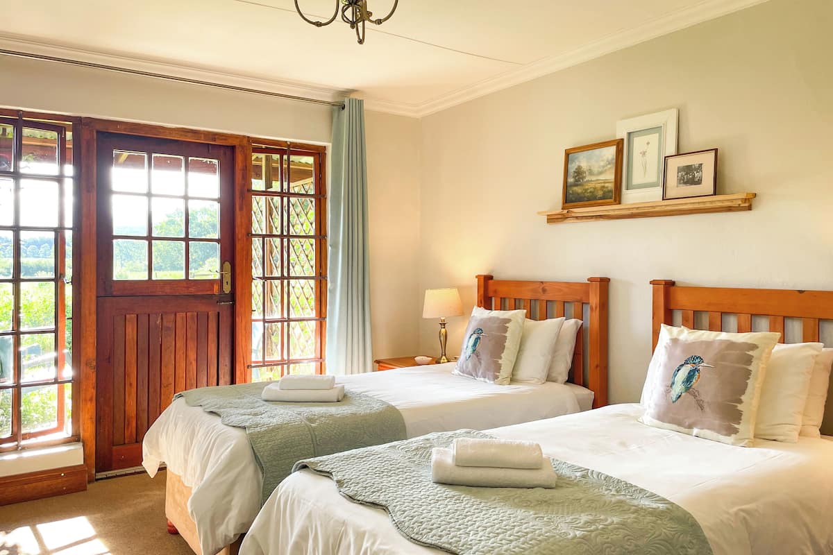 A bedroom with two beds, a wooden door, a window with curtains, and a wall-mounted shelf with pictures.