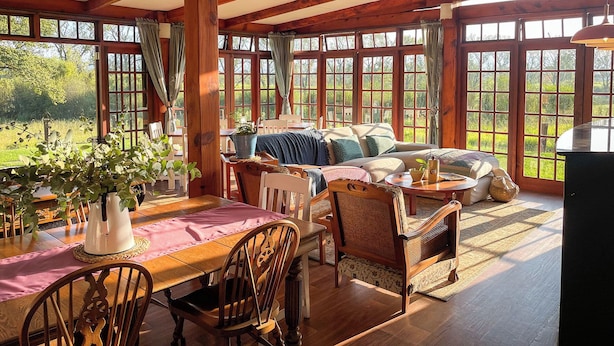A spacious room with a wooden ceiling, large windows, a dining area with a table and chairs, and a cozy seating area with a sofa and cushions. - Molweni Kamberg Valley Bed and Breakfast (Elandskop)